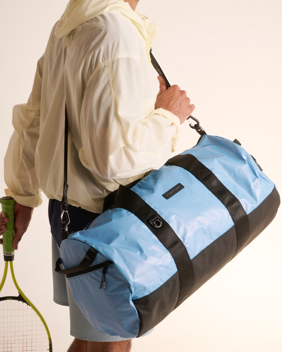 Person carrying the blue Weekender duffle, the best beach bag for travel